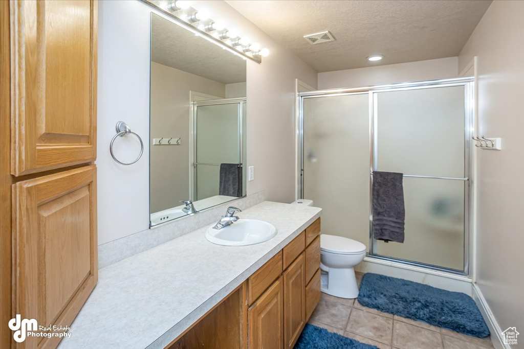 Bathroom featuring tile patterned flooring, a textured ceiling, a shower with door, vanity, and toilet