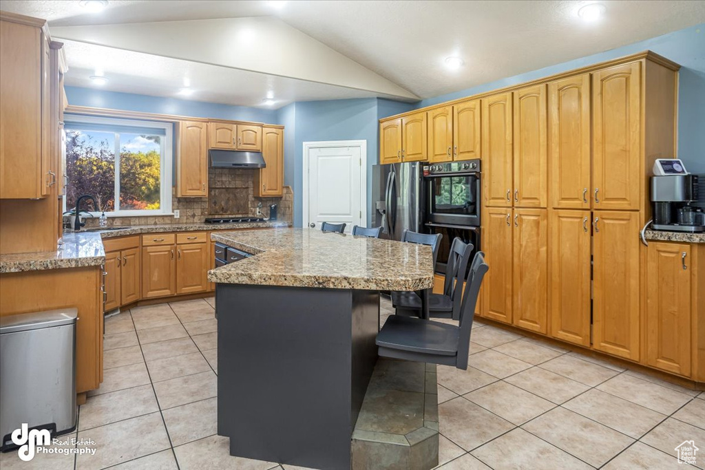 Kitchen featuring light stone counters, a kitchen island, light tile patterned floors, lofted ceiling, and sink