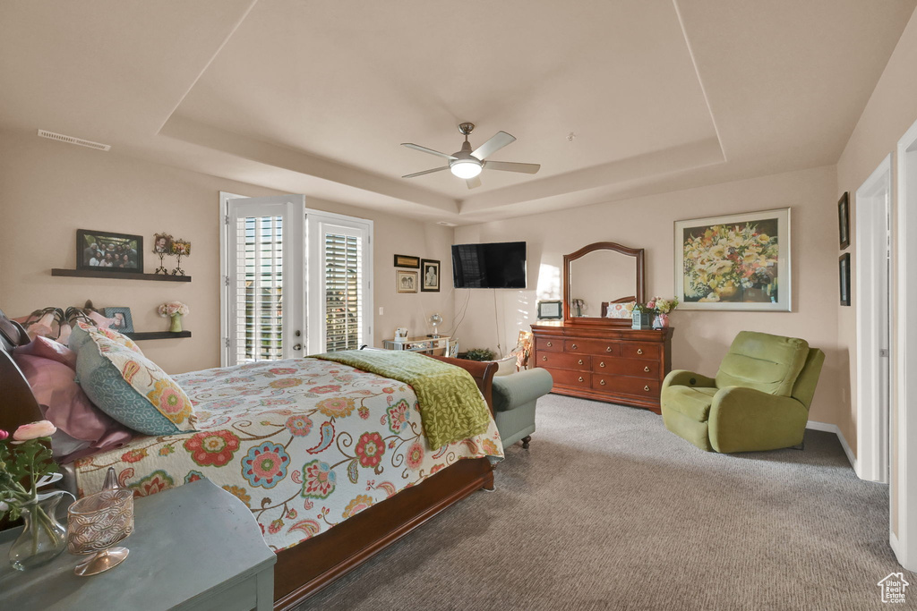 Bedroom with ceiling fan, a raised ceiling, access to exterior, and carpet