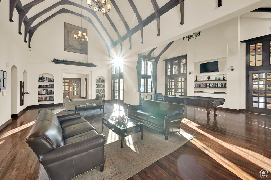 Living room with pool table, dark hardwood / wood-style floors, a notable chandelier, high vaulted ceiling, and built in features