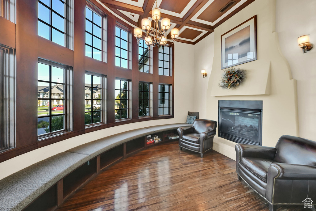 Living room featuring coffered ceiling, beamed ceiling, wood-type flooring, a high ceiling, and a chandelier