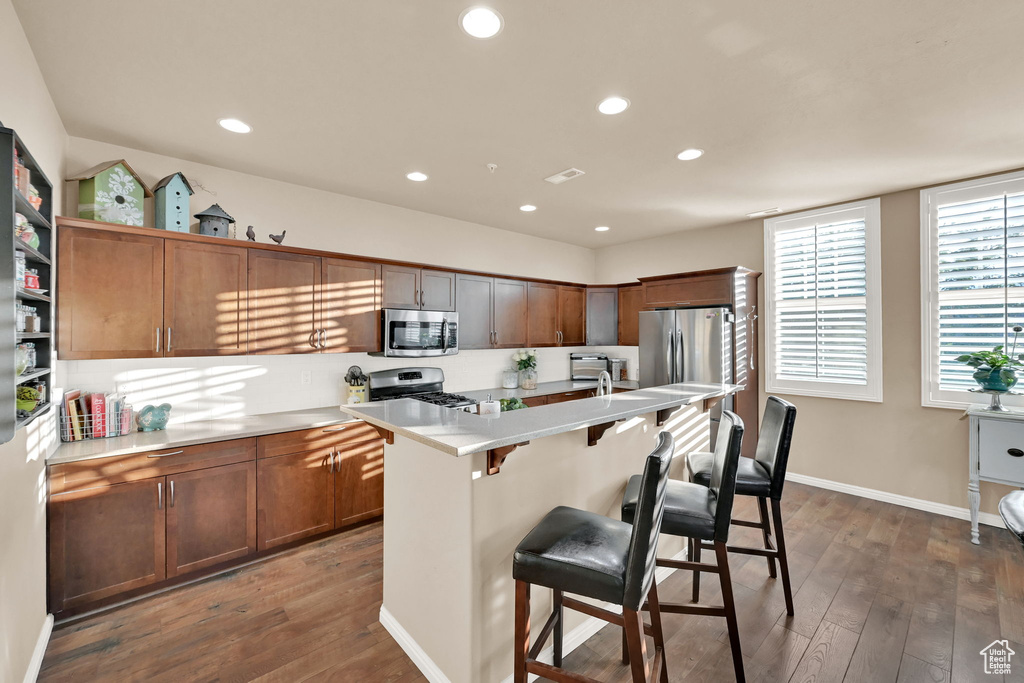 Kitchen with a kitchen breakfast bar, a center island with sink, appliances with stainless steel finishes, and dark hardwood / wood-style flooring