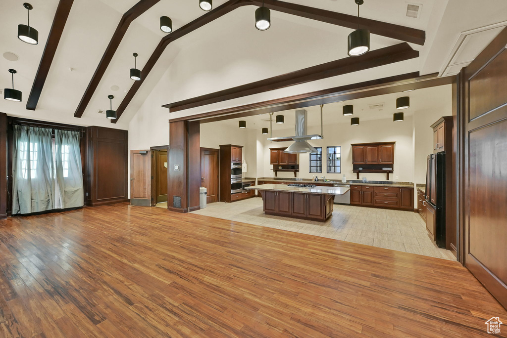 Kitchen featuring high vaulted ceiling, pendant lighting, light wood-type flooring, beam ceiling, and a center island