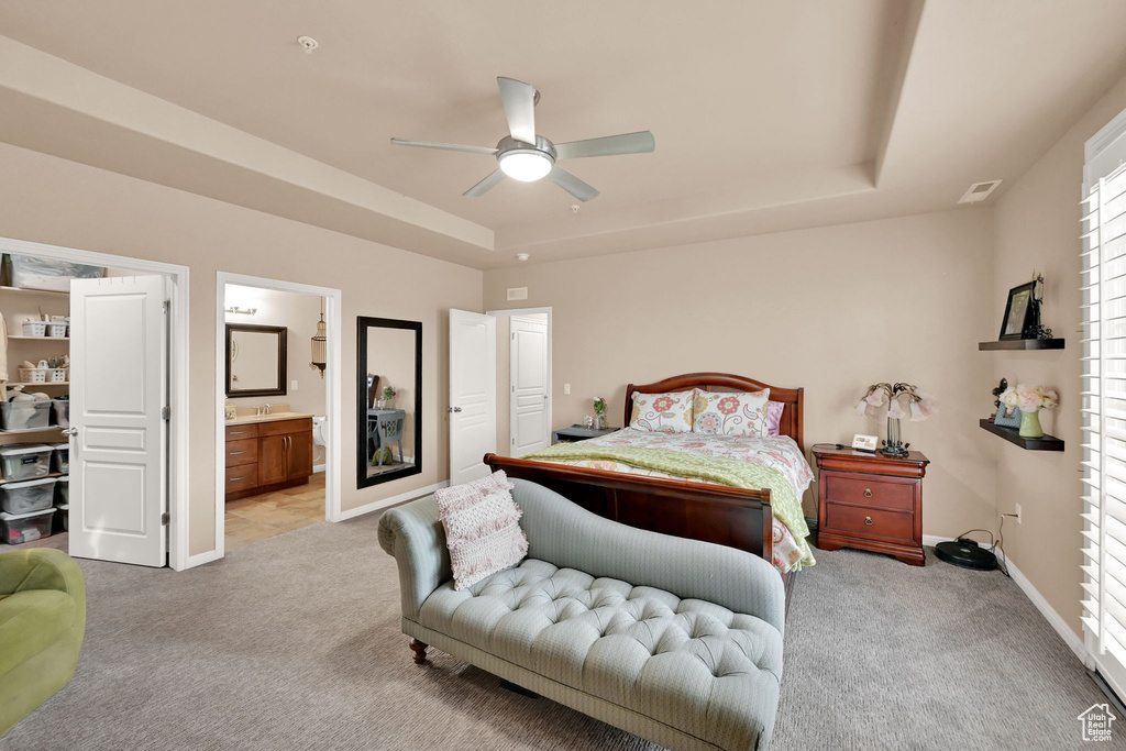 Bedroom with a raised ceiling, ensuite bath, ceiling fan, and light colored carpet