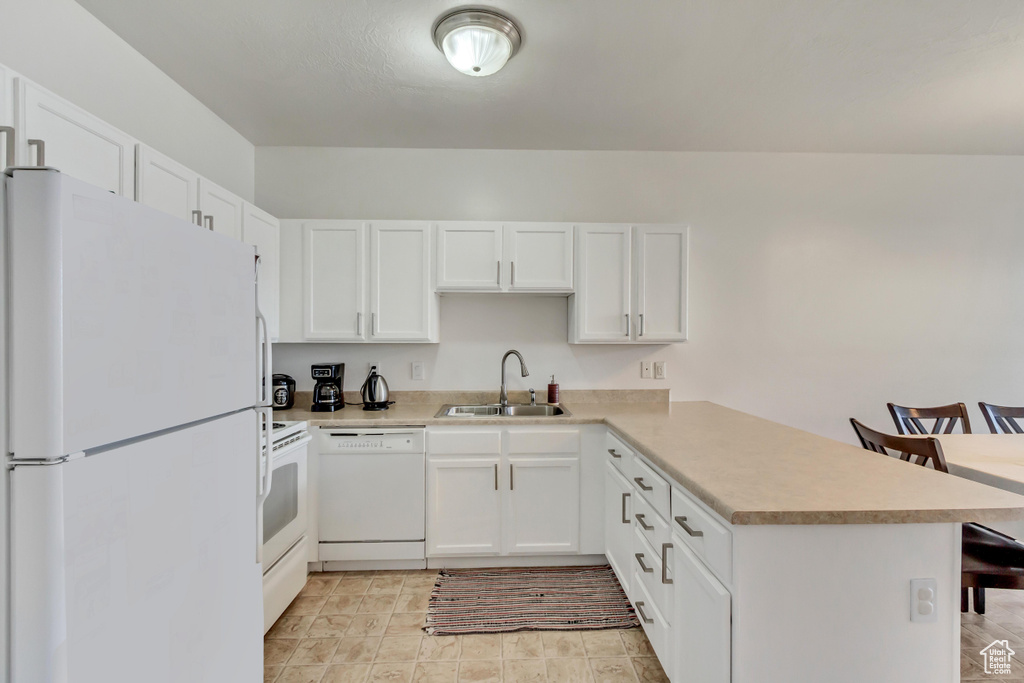 Kitchen with white appliances, sink, white cabinets, and kitchen peninsula