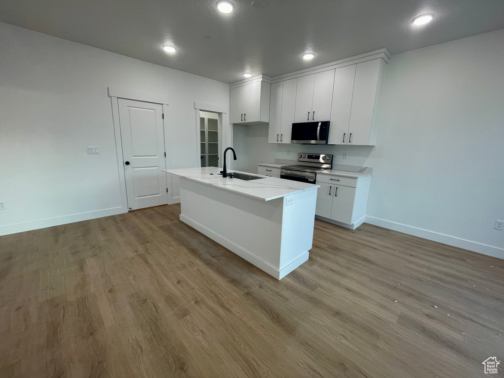 Kitchen with an island with sink, stainless steel appliances, sink, white cabinets, and light hardwood / wood-style floors