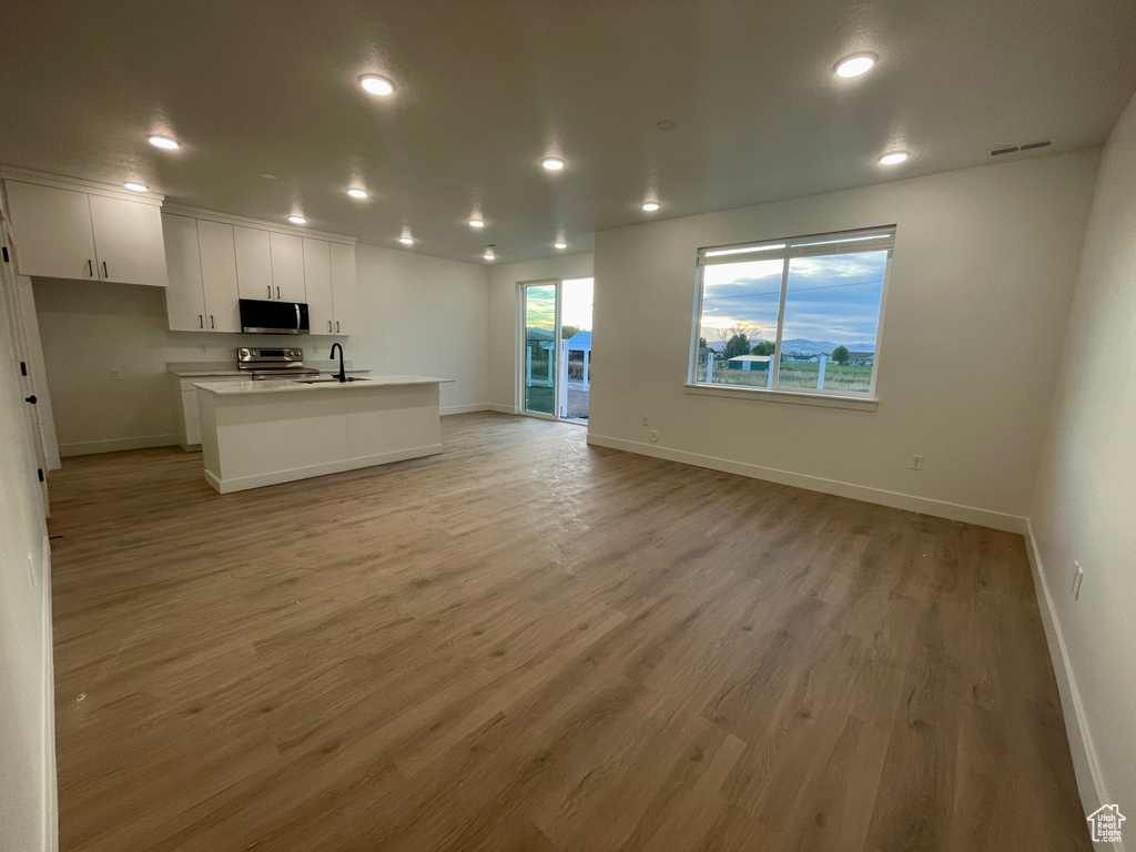 Kitchen featuring an island with sink, white cabinetry, light hardwood / wood-style flooring, sink, and stainless steel appliances