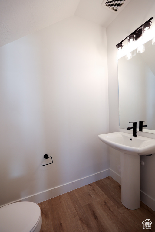 Bathroom featuring vaulted ceiling, sink, hardwood / wood-style floors, and toilet