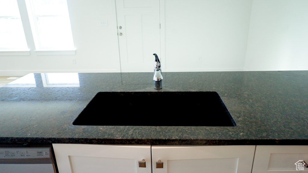 Room details featuring dark stone counters, white cabinets, dishwasher, and sink