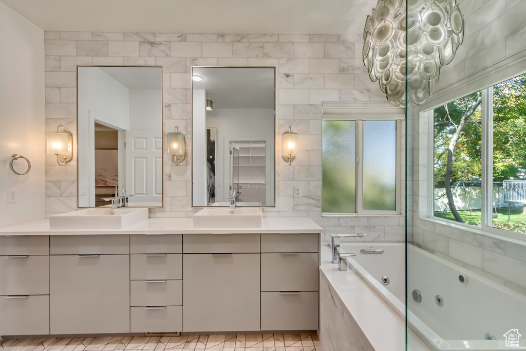 Bathroom featuring tiled tub, vanity, a chandelier, and a wealth of natural light