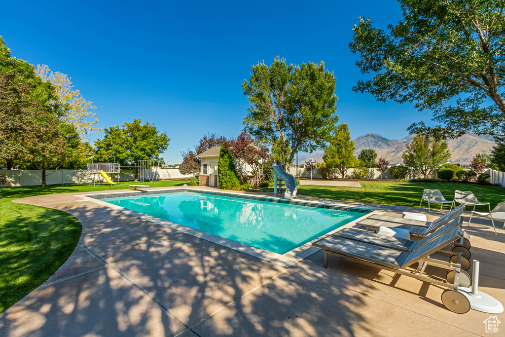 View of swimming pool featuring a mountain view, a patio area, a diving board, a water slide, and a yard