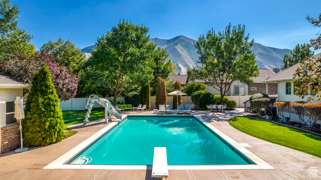 View of pool featuring a mountain view, a lawn, a water slide, a patio area, and a diving board