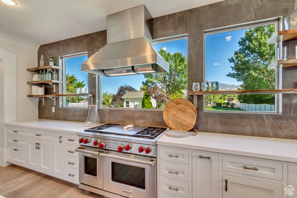 Kitchen with white cabinetry, light hardwood / wood-style flooring, range with two ovens, backsplash, and exhaust hood