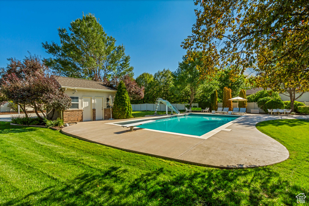 View of swimming pool featuring a patio, a diving board, a lawn, and a water slide