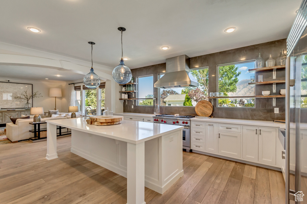 Kitchen with white cabinets, luxury range, light hardwood / wood-style flooring, backsplash, and extractor fan