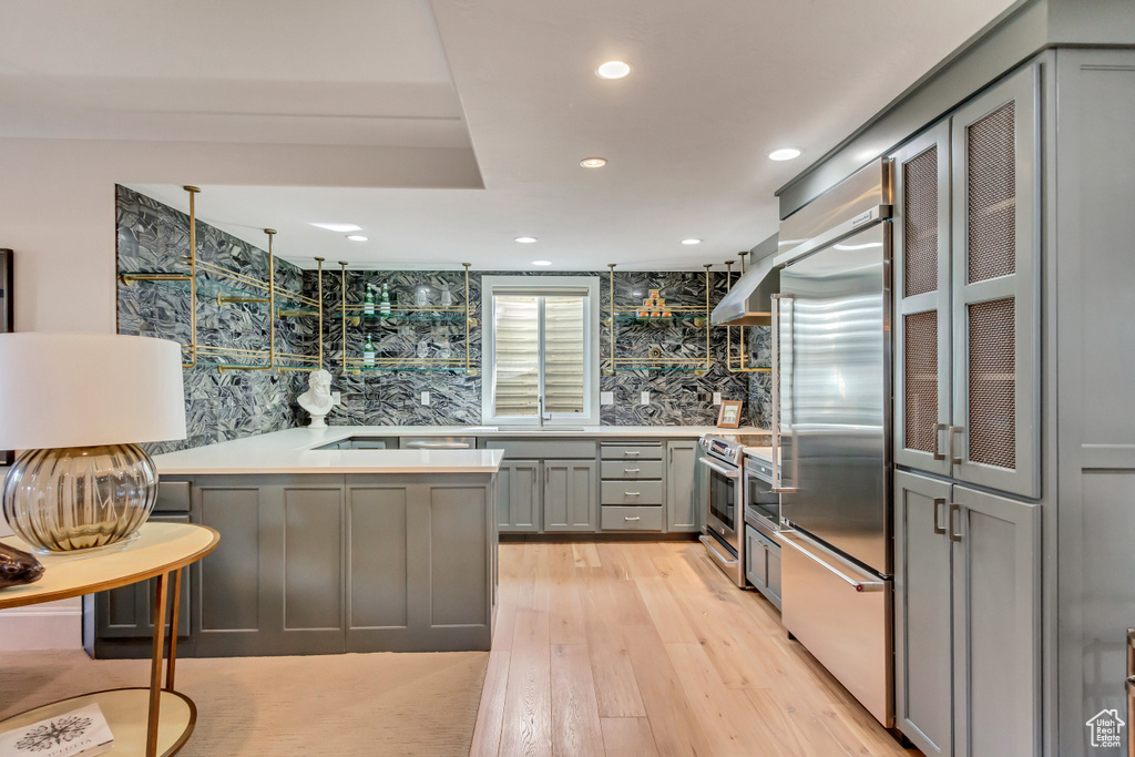 Kitchen featuring tasteful backsplash, gray cabinetry, exhaust hood, stainless steel appliances, and light wood-type flooring