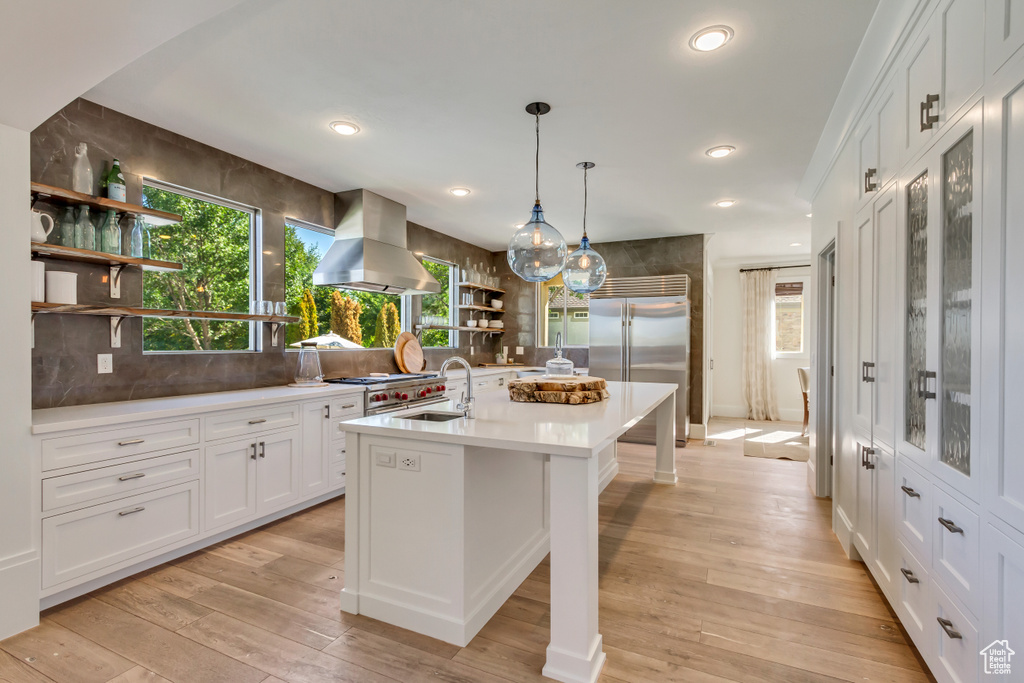 Kitchen featuring ventilation hood, light hardwood / wood-style floors, white cabinetry, and an island with sink