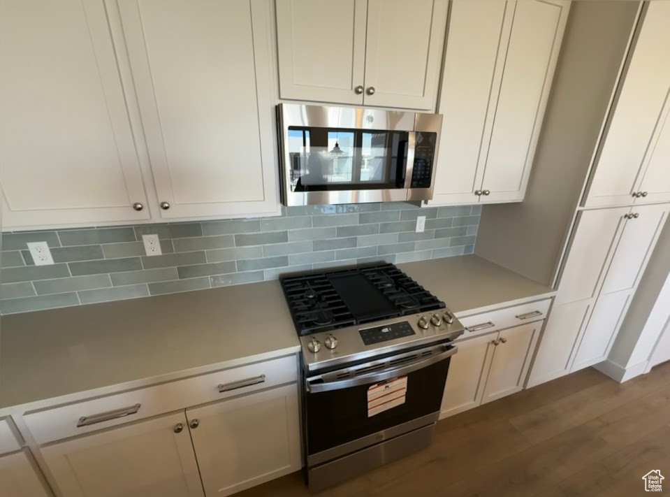 Kitchen featuring decorative backsplash, stainless steel appliances, white cabinetry, and hardwood / wood-style floors