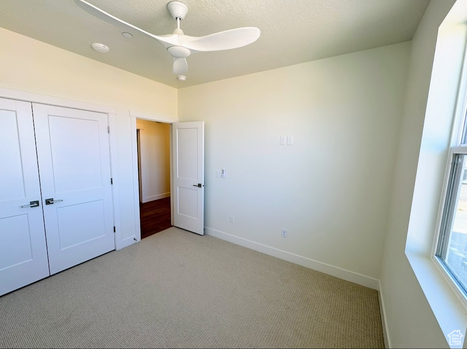 Unfurnished bedroom with ceiling fan, light colored carpet, a textured ceiling, and a closet