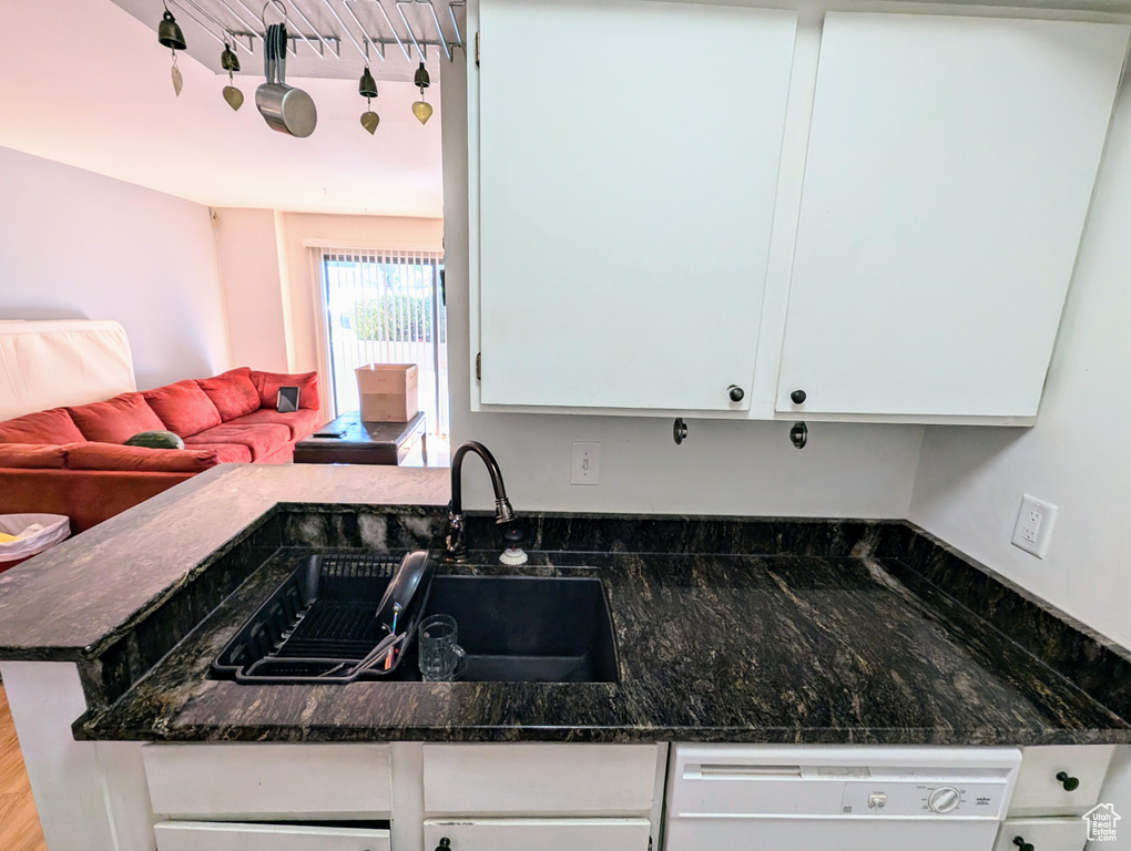 Kitchen featuring white cabinets, white dishwasher, sink, kitchen peninsula, and dark stone countertops