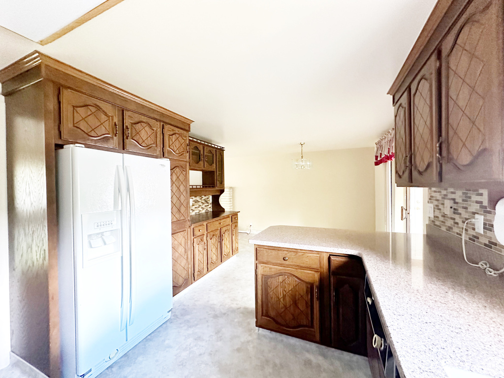 Kitchen with hanging light fixtures, kitchen peninsula, backsplash, and white refrigerator with ice dispenser