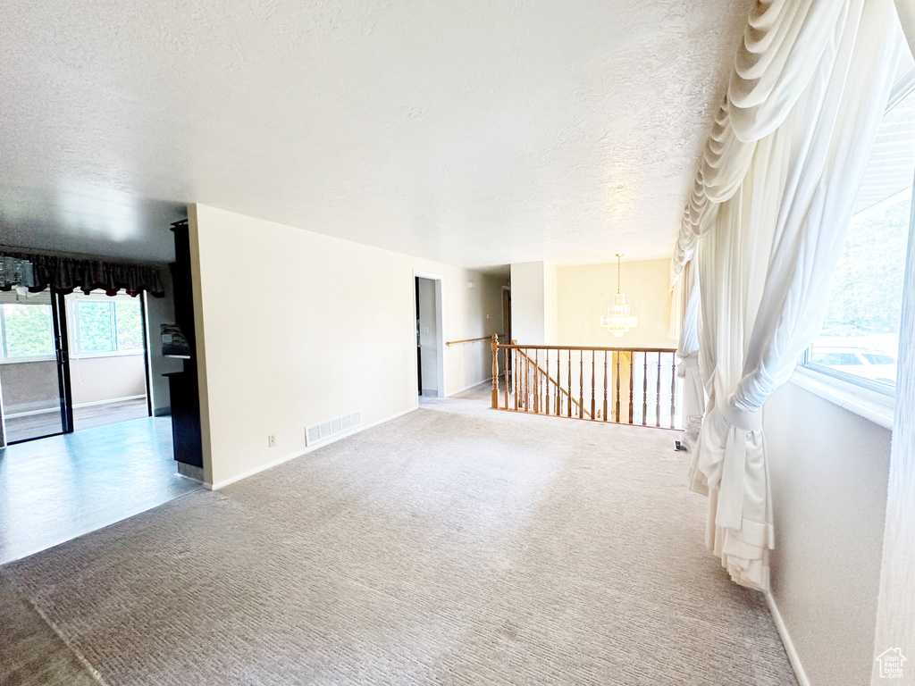 Carpeted spare room featuring a textured ceiling and a chandelier