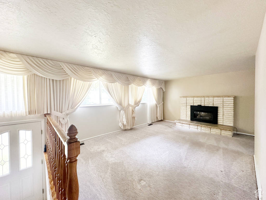 Unfurnished living room featuring carpet floors, a textured ceiling, and a fireplace