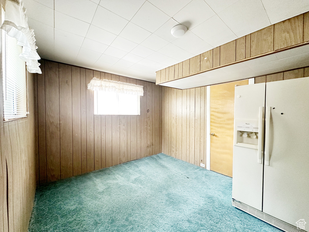 Basement featuring wooden walls, white fridge with ice dispenser, and carpet flooring