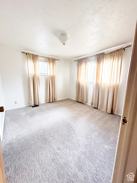 Spare room featuring a textured ceiling, carpet, and a healthy amount of sunlight