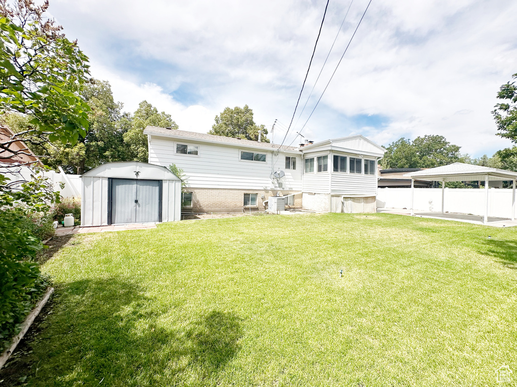 Rear view of property with a shed, a carport, and a lawn