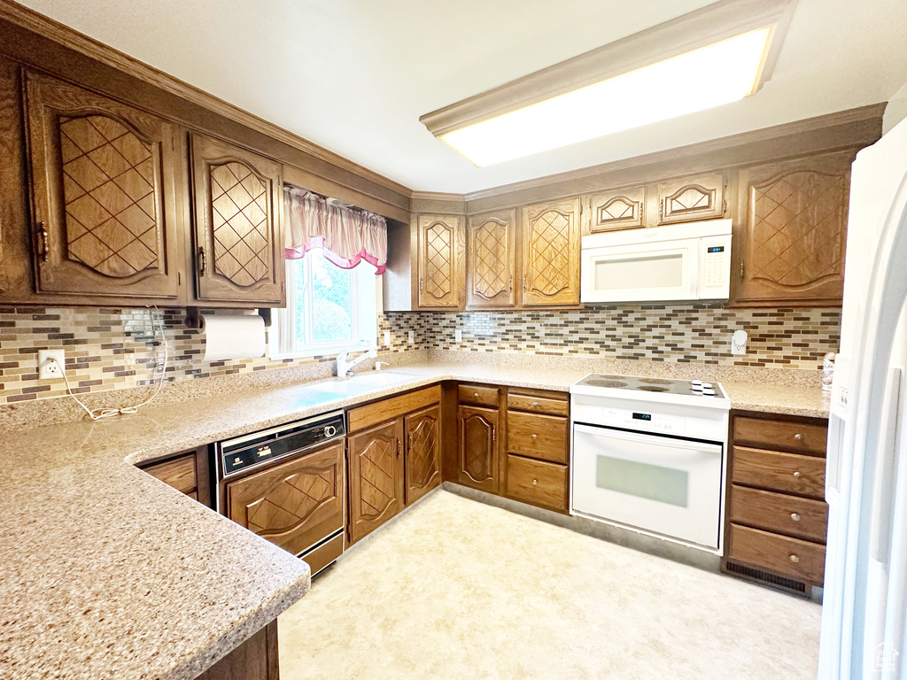 Kitchen with light stone counters, sink, white appliances, backsplash, and light colored carpet