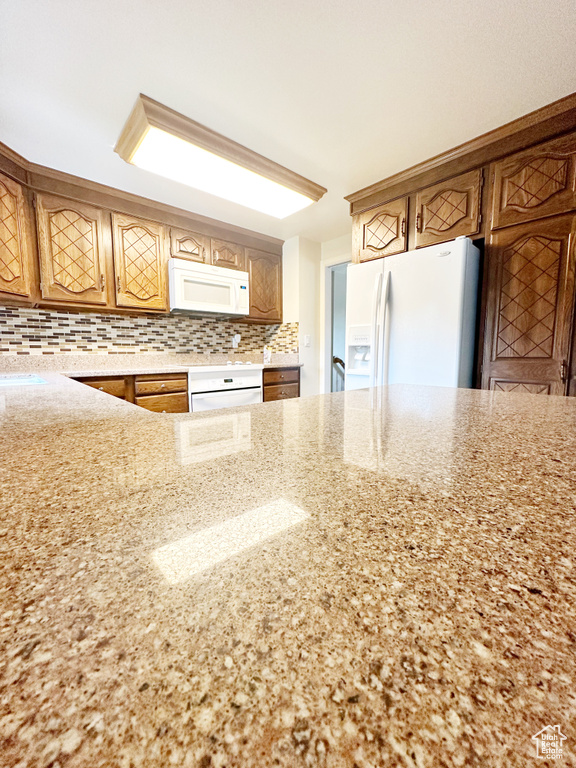 Kitchen featuring backsplash, white appliances, and light stone counters