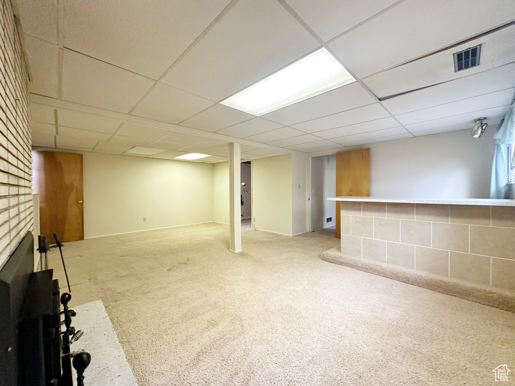 Basement with light colored carpet, a fireplace, and a drop ceiling