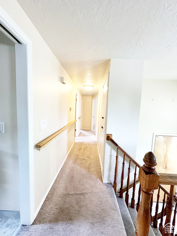 Corridor featuring light carpet and a textured ceiling