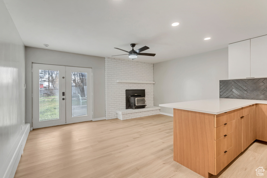 Kitchen featuring light wood-type flooring, kitchen peninsula, a fireplace, and ceiling fan