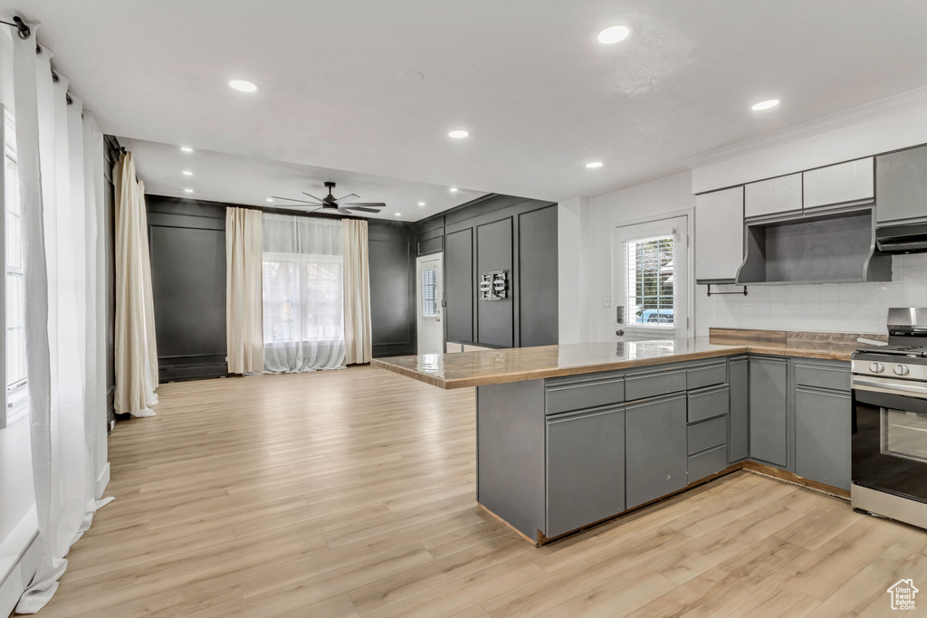 Kitchen featuring stainless steel stove, kitchen peninsula, gray cabinetry, and ceiling fan