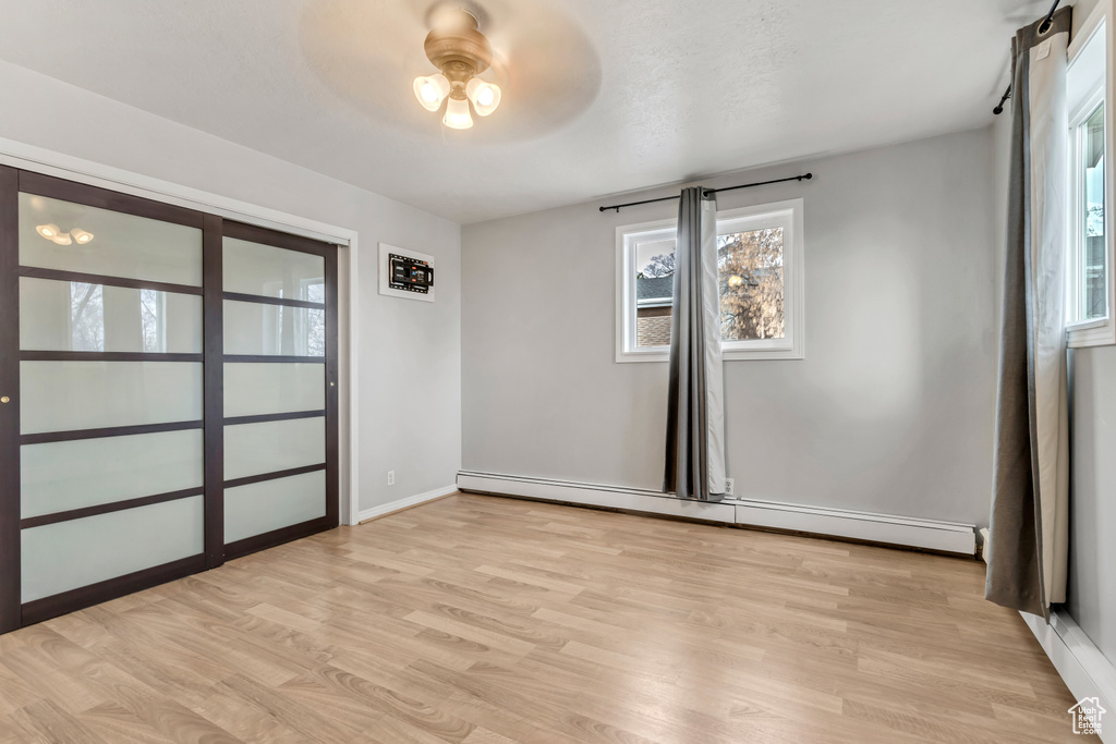 Empty room with a healthy amount of sunlight, light hardwood / wood-style floors, a baseboard heating unit, and ceiling fan