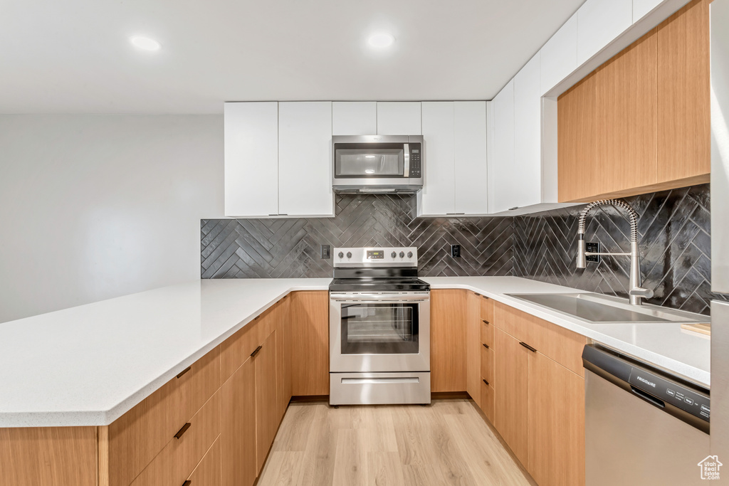 Kitchen featuring sink, stainless steel appliances, light hardwood / wood-style floors, and white cabinetry