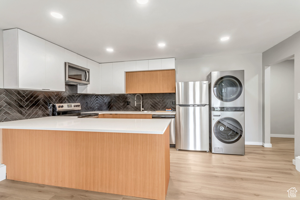 Kitchen with white cabinets, sink, stacked washer and clothes dryer, light hardwood / wood-style flooring, and appliances with stainless steel finishes