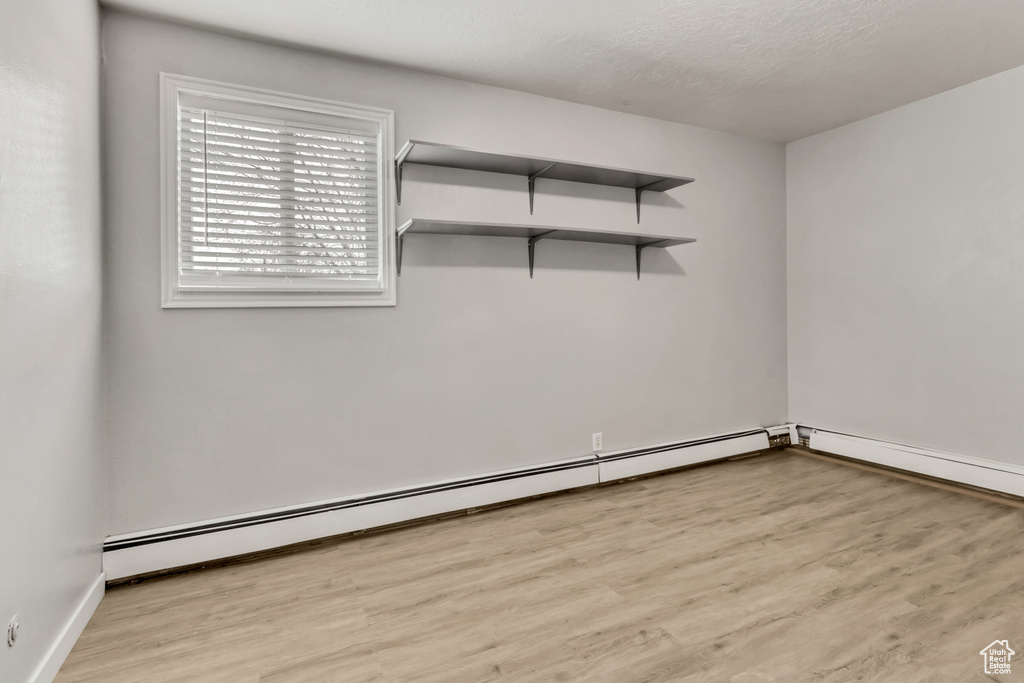 Unfurnished room featuring a baseboard radiator, light hardwood / wood-style floors, and a textured ceiling