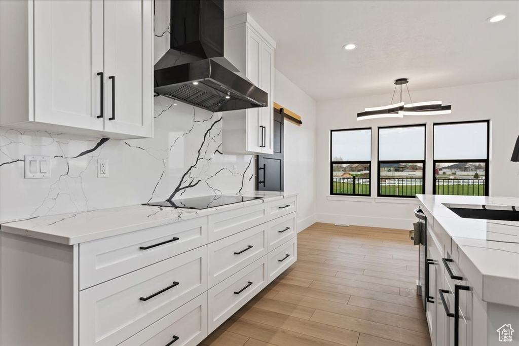 Kitchen featuring backsplash, wall chimney range hood, light stone counters, and white cabinets