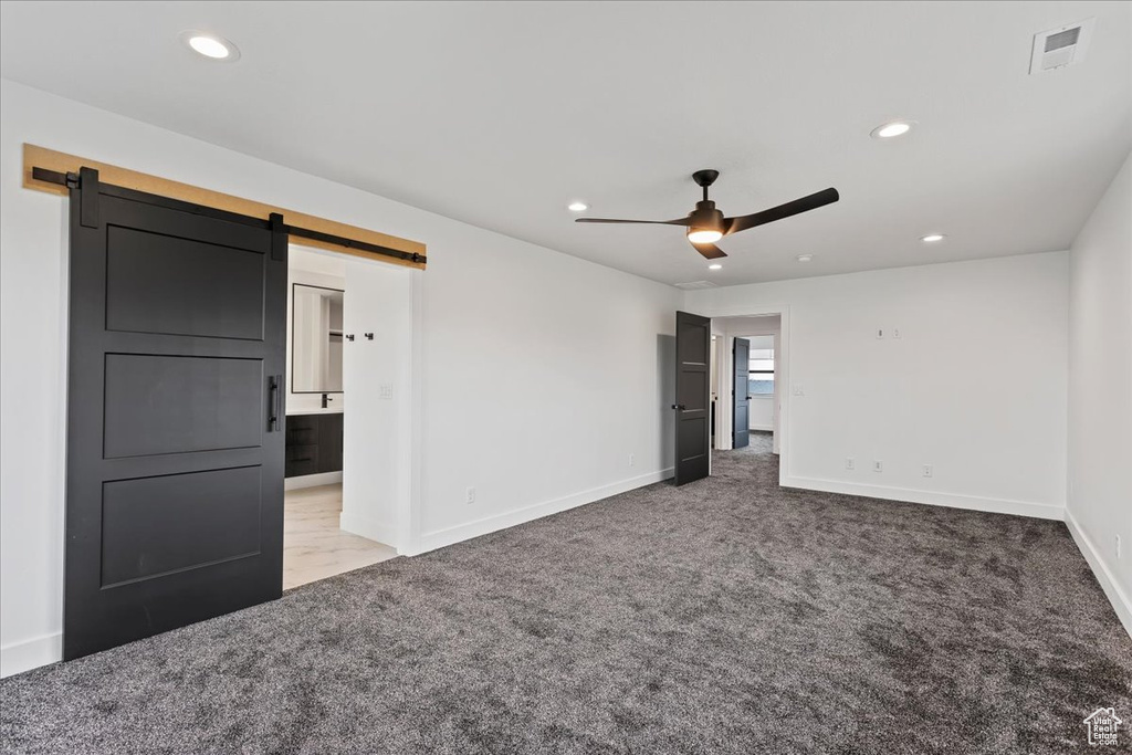 Unfurnished room featuring ceiling fan, carpet floors, and a barn door