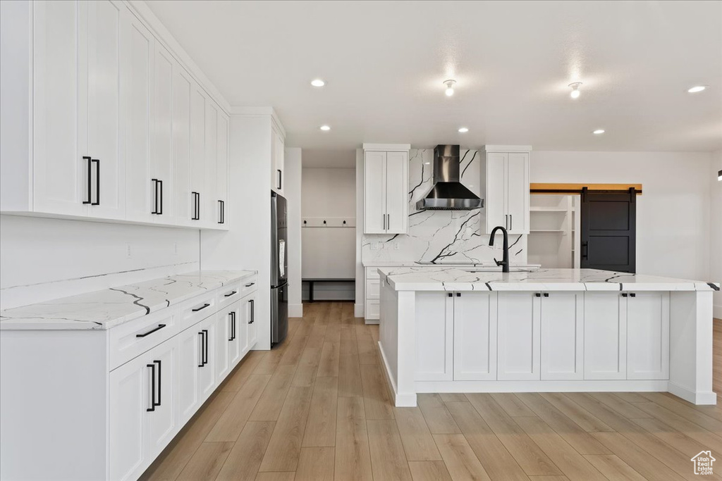 Kitchen featuring white cabinets, wall chimney range hood, a barn door, light hardwood / wood-style flooring, and light stone countertops