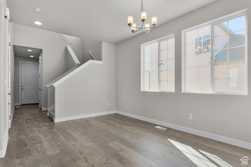 Empty room featuring an inviting chandelier, hardwood / wood-style flooring, and a wealth of natural light