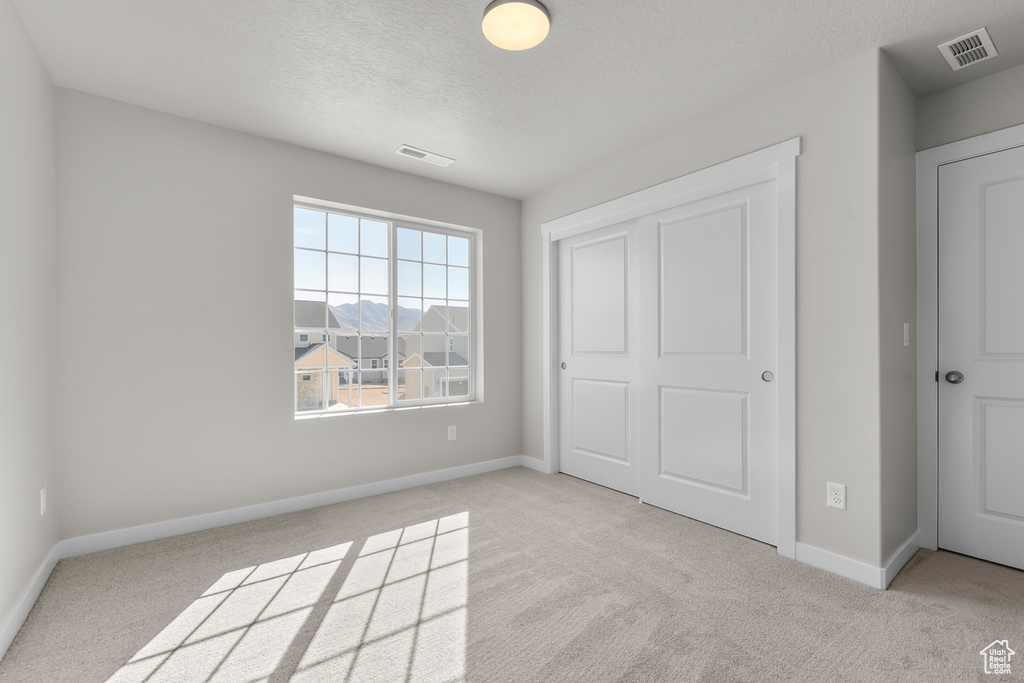 Unfurnished bedroom with a closet, a textured ceiling, and light colored carpet