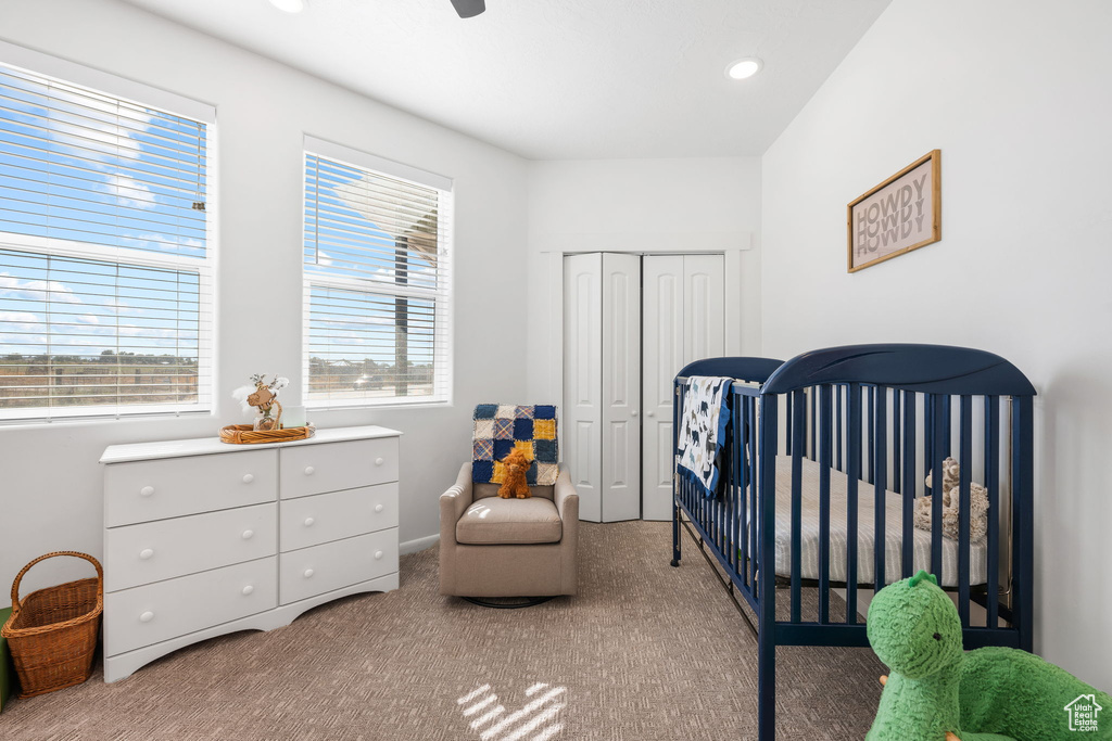 Bedroom with a crib, carpet flooring, ceiling fan, and a closet