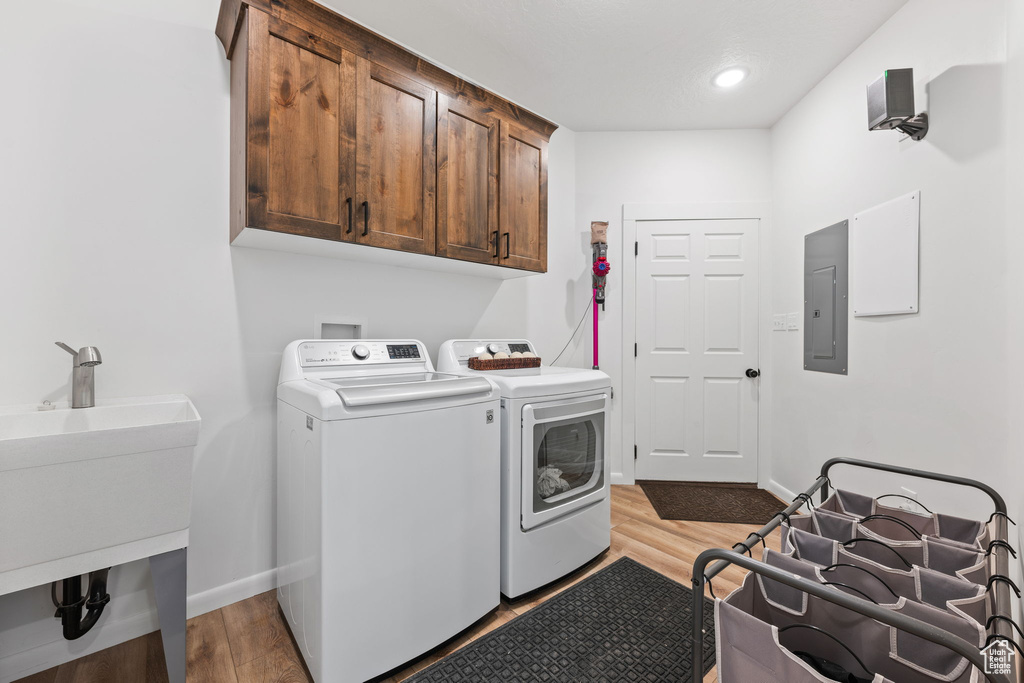 Clothes washing area featuring independent washer and dryer, light wood-type flooring, cabinets, electric panel, and sink