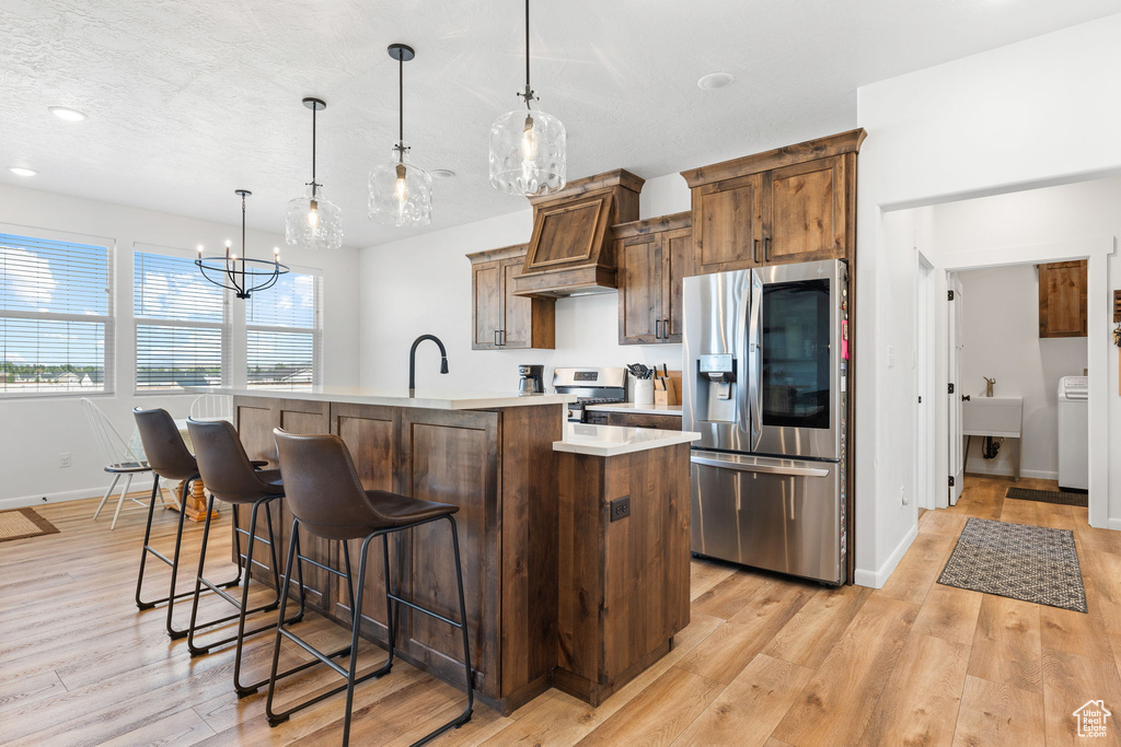 Kitchen with appliances with stainless steel finishes, a center island with sink, pendant lighting, and light hardwood / wood-style flooring