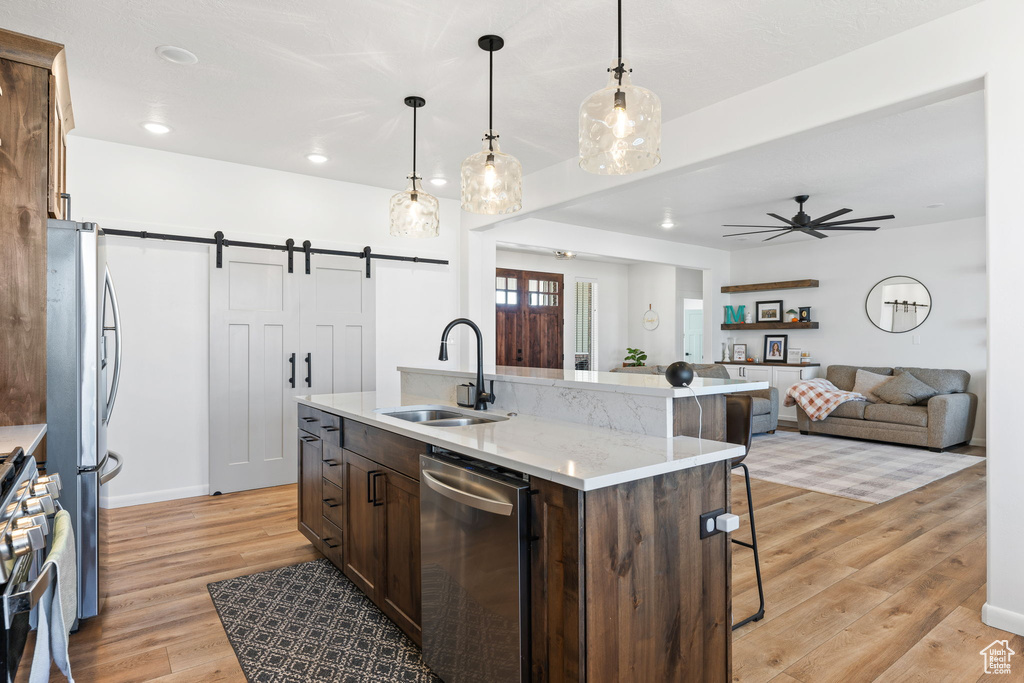 Kitchen with a barn door, a breakfast bar area, stainless steel appliances, light wood-type flooring, and sink