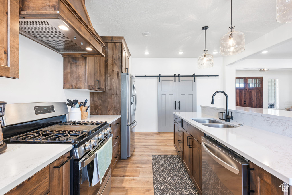 Kitchen with custom exhaust hood, decorative light fixtures, appliances with stainless steel finishes, a barn door, and light hardwood / wood-style floors